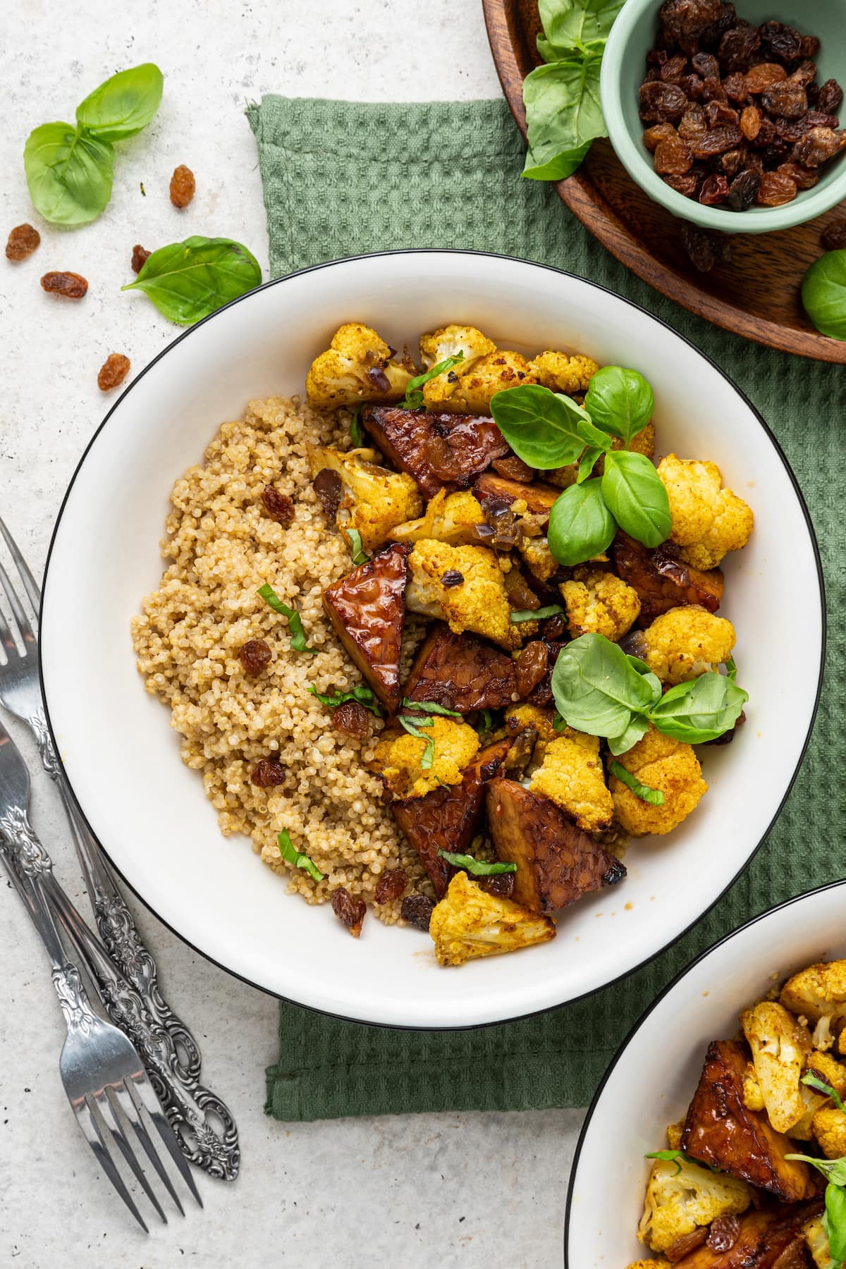 A white bowl containing the curried cauliflower and tempeh over a bed of quinoa and garnished with fresh basil leaves.