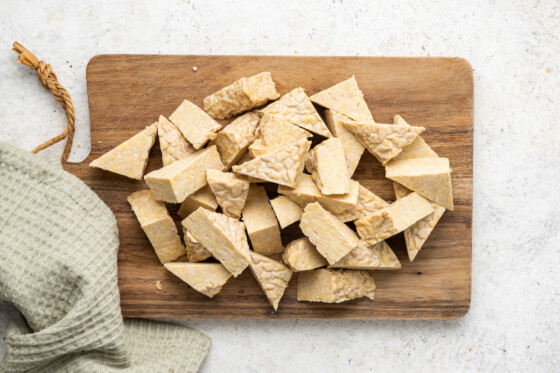 Tempeh cut into triangles on top of a medium-sized wooden cutting board.