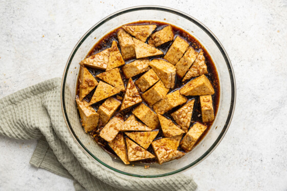 Tempeh cut into triangles marinating in a large glass bowl.