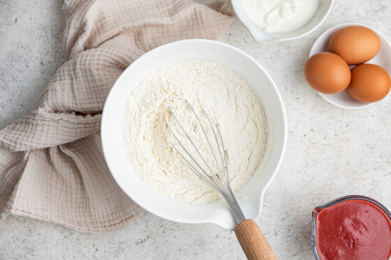 White flour inside a white bowl with a whisk.