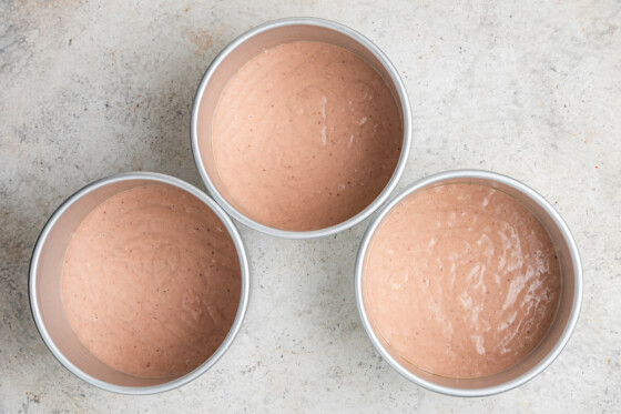 Three layers of cake in three separate round pans with strawberry cake filling on top.