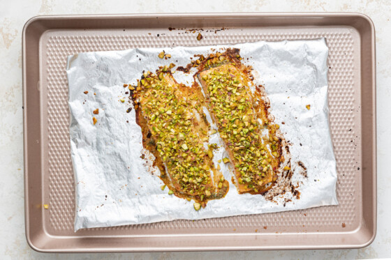 Two baked salmon filets topped with chopped pistachios on a baking tray.