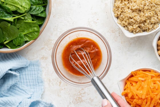 A womans hand using a whisk to whisk the spicy harissa dressing.