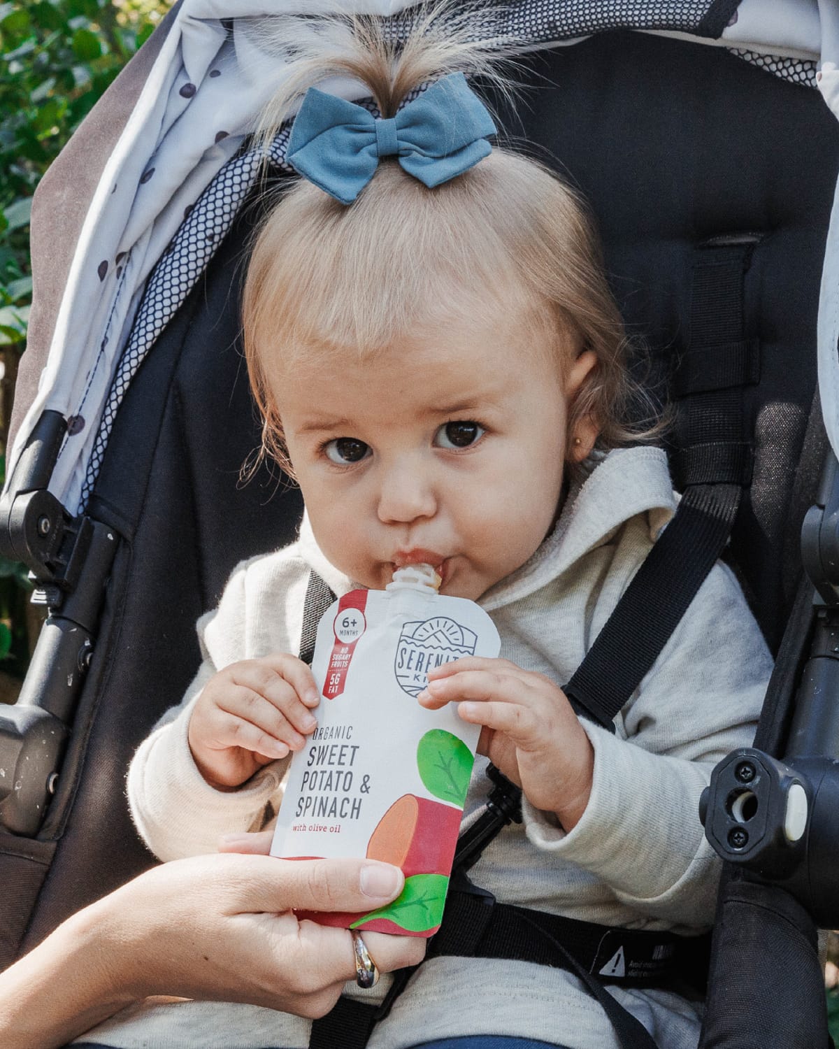 Baby girl in a stroller eating a serenity kids pouch.
