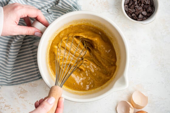 A woman's hand holds a whisk while whisking the wet ingredients of the tahini banana bread recipe.
