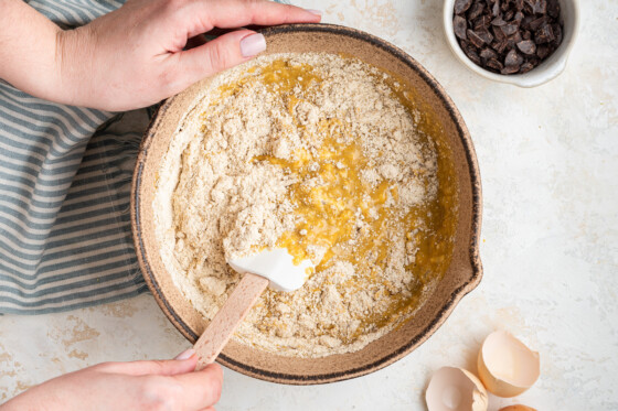 A woman's hand holds a silicon spatula while mixing the dry ingredients of the tahini banana bread.