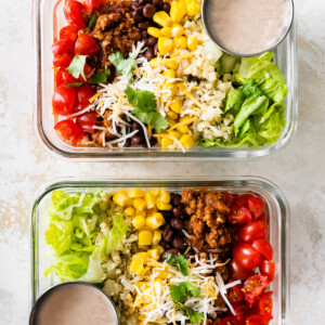 Two turkey taco bowls in glass storage containers for meal prep served with a side of dressing.