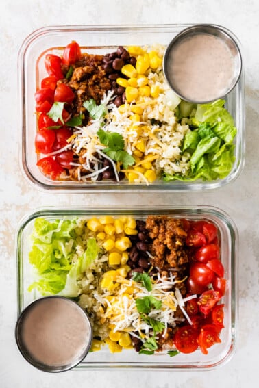 Two turkey taco bowls in glass storage containers for meal prep served with a side of dressing.