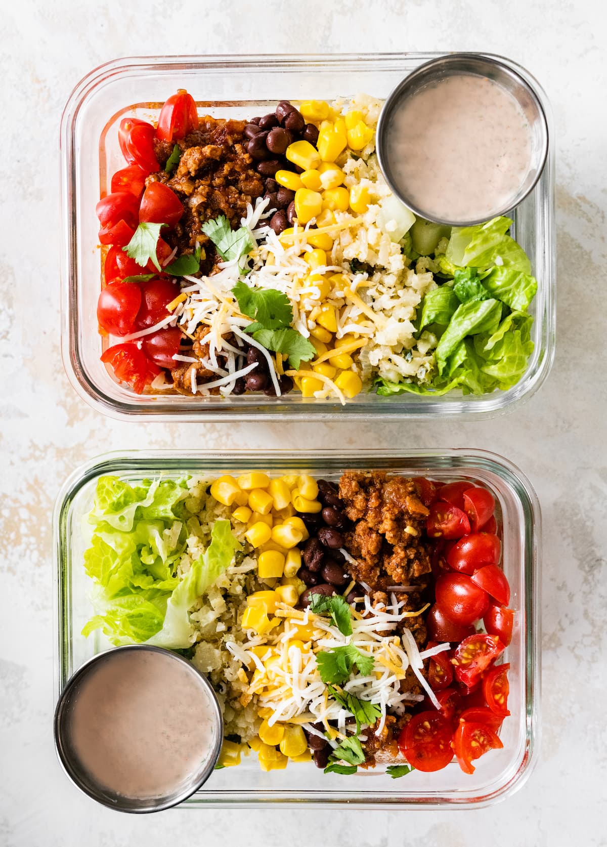 Two turkey taco bowls in glass storage containers for meal prep served with a side of dressing.