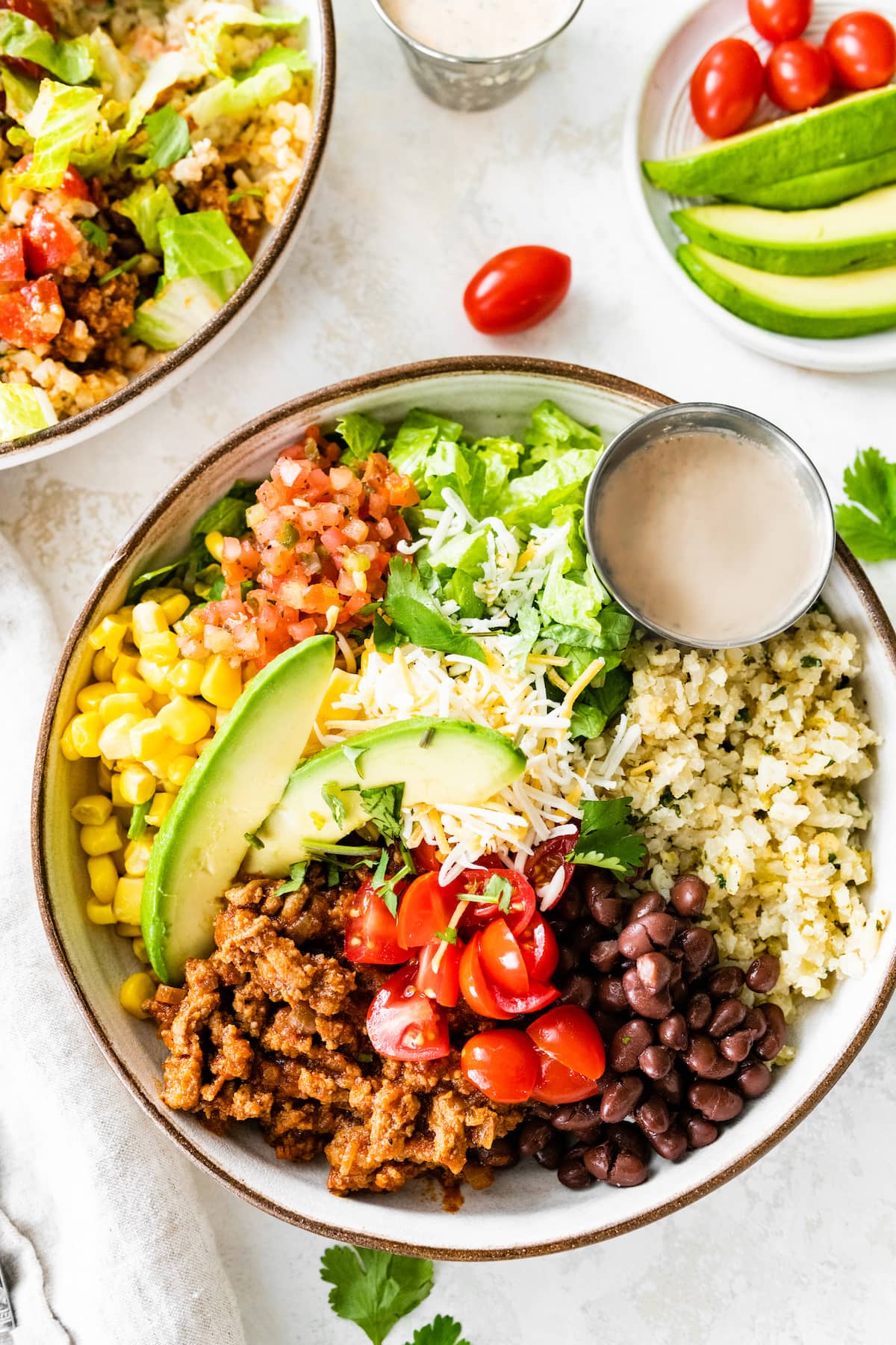 Turkey taco bowl served in a white serving bowl, topped with avocado, cheese and served with a side of dressing.