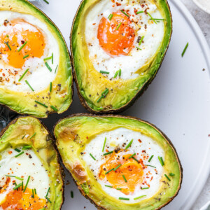 On a white plate, two halved avocados with an egg in the center, each recently baked.