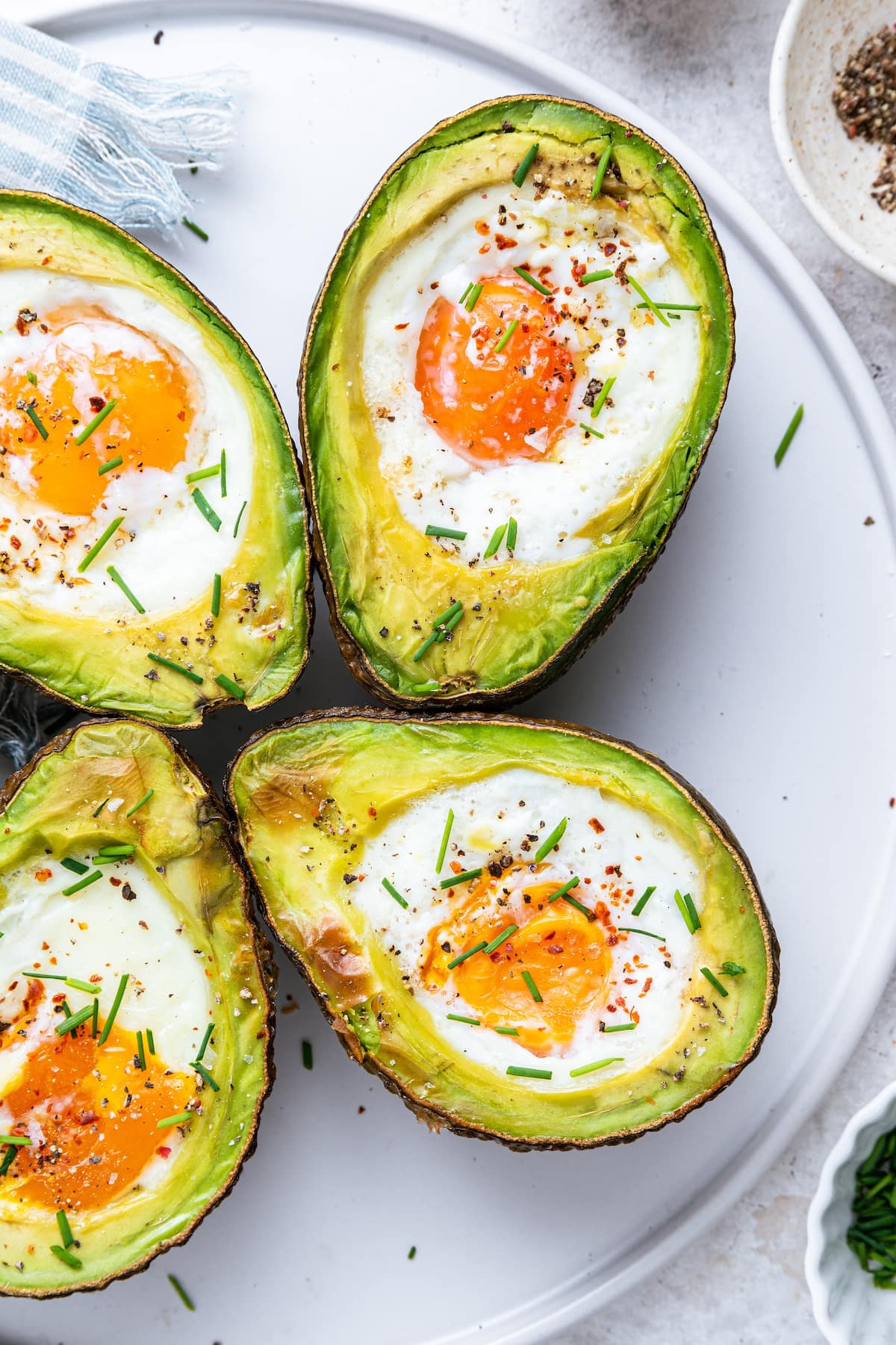 On a white plate, two halved avocados with an egg in the center, each recently baked.