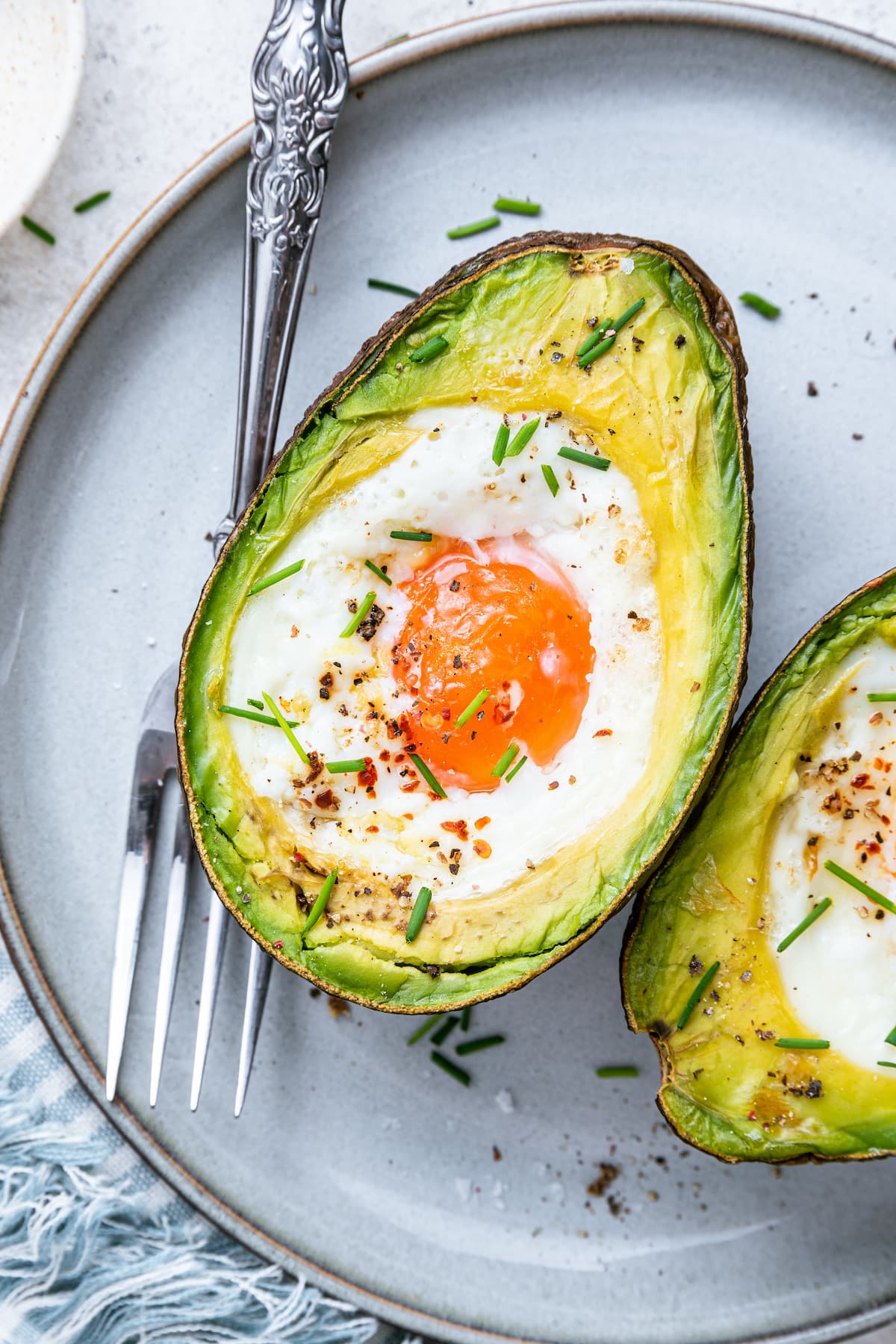 A baked avocado with an egg in the center on a plate with a fork.