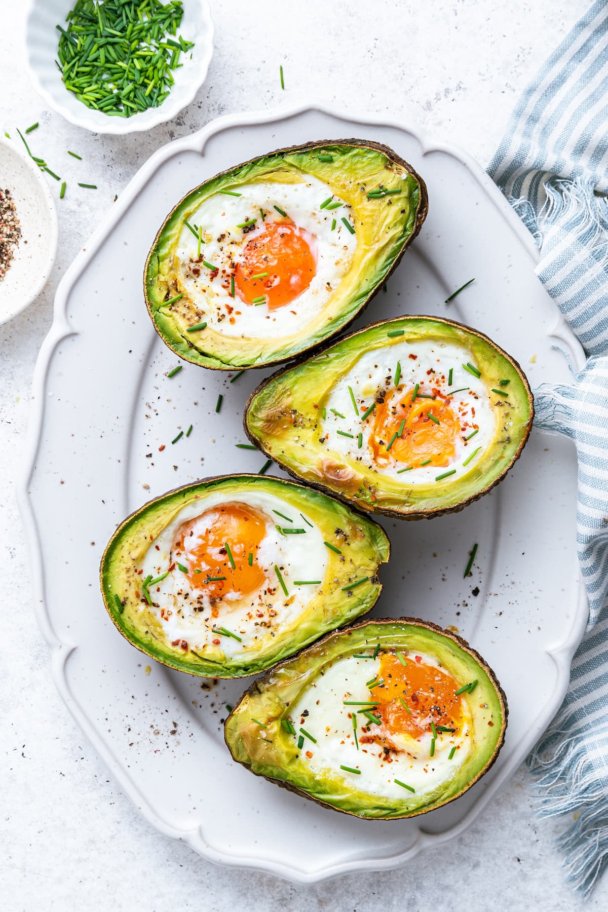 On a white plate, two halved avocados with an egg in the center, each recently baked.