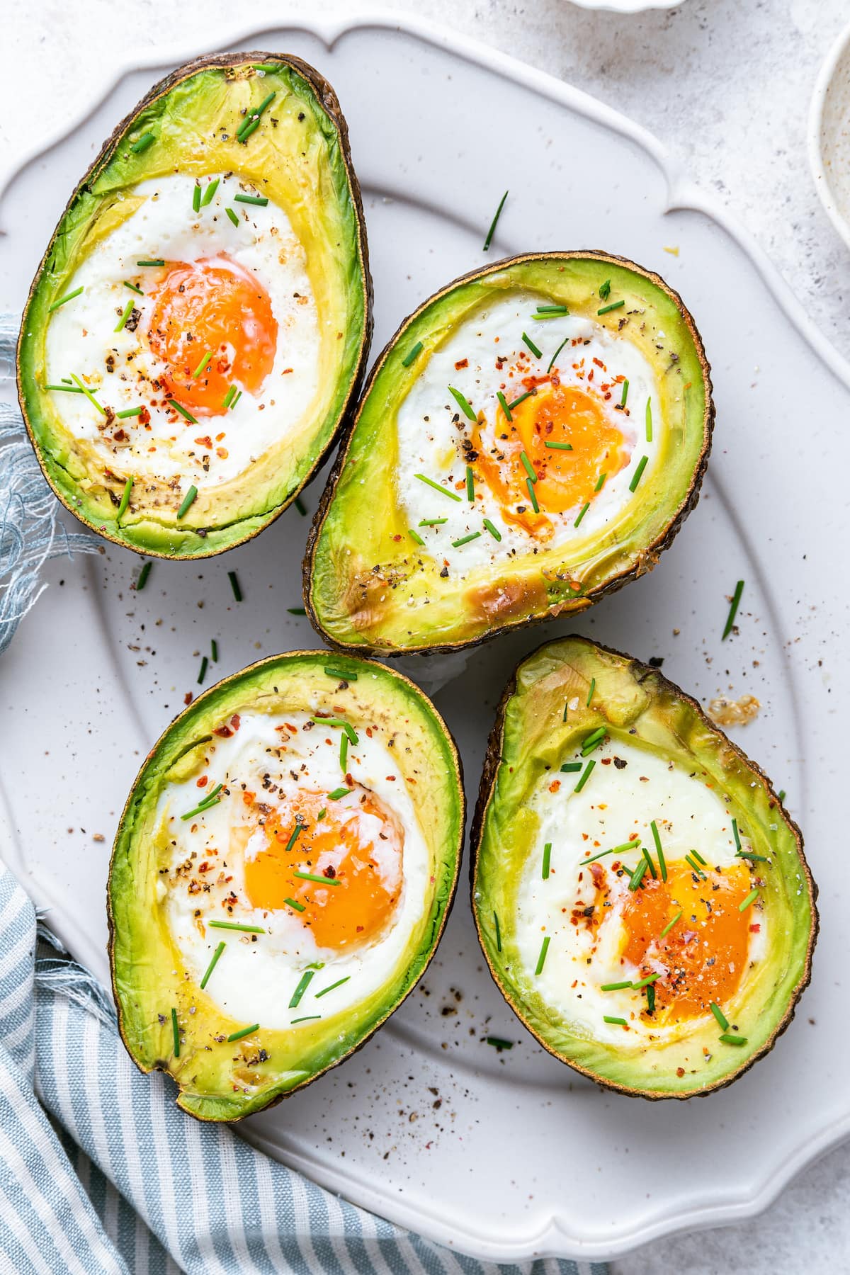 On a white plate, two halved avocados with an egg in the center, each recently baked.