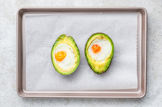 A baked avocado with two eggs inside of each half on a baking tray.