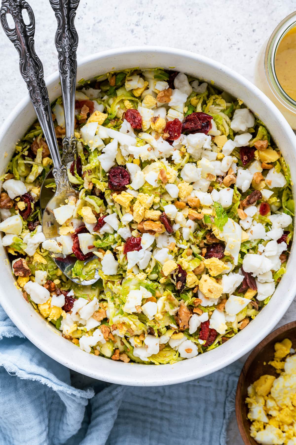 A large white bowl with two metal serving spoons containing the Brussels sprout chopped salad.