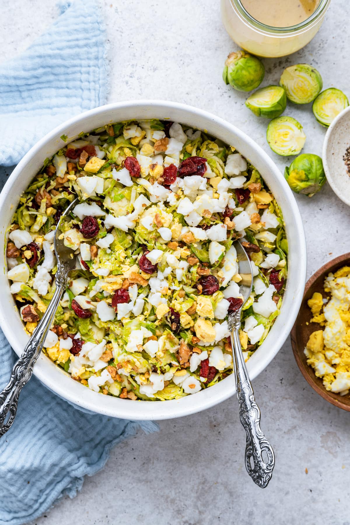 A large white bowl with two metal serving spoons containing the Brussels sprout chopped salad.