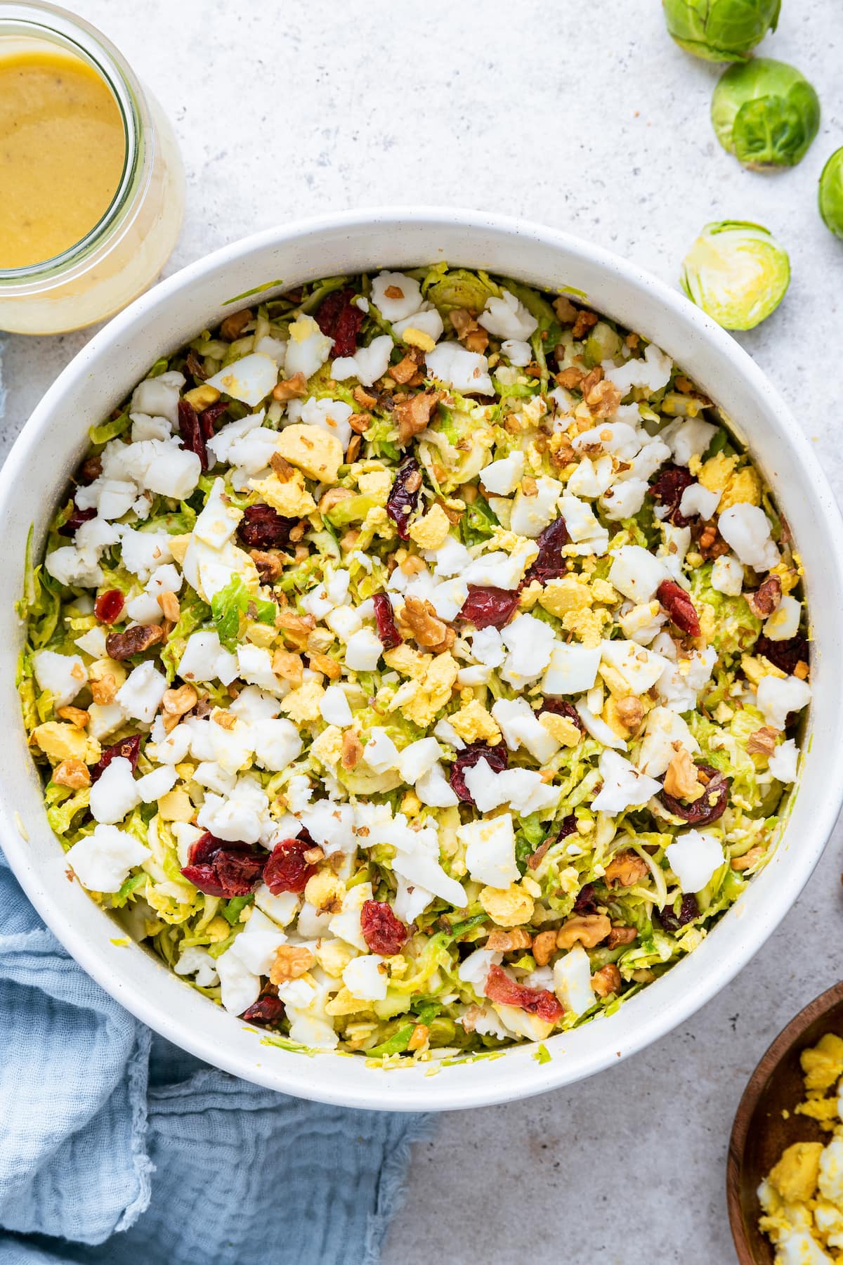 A large white bowl containing the Brussels sprout chopped salad, topped with crumbled goat cheese.