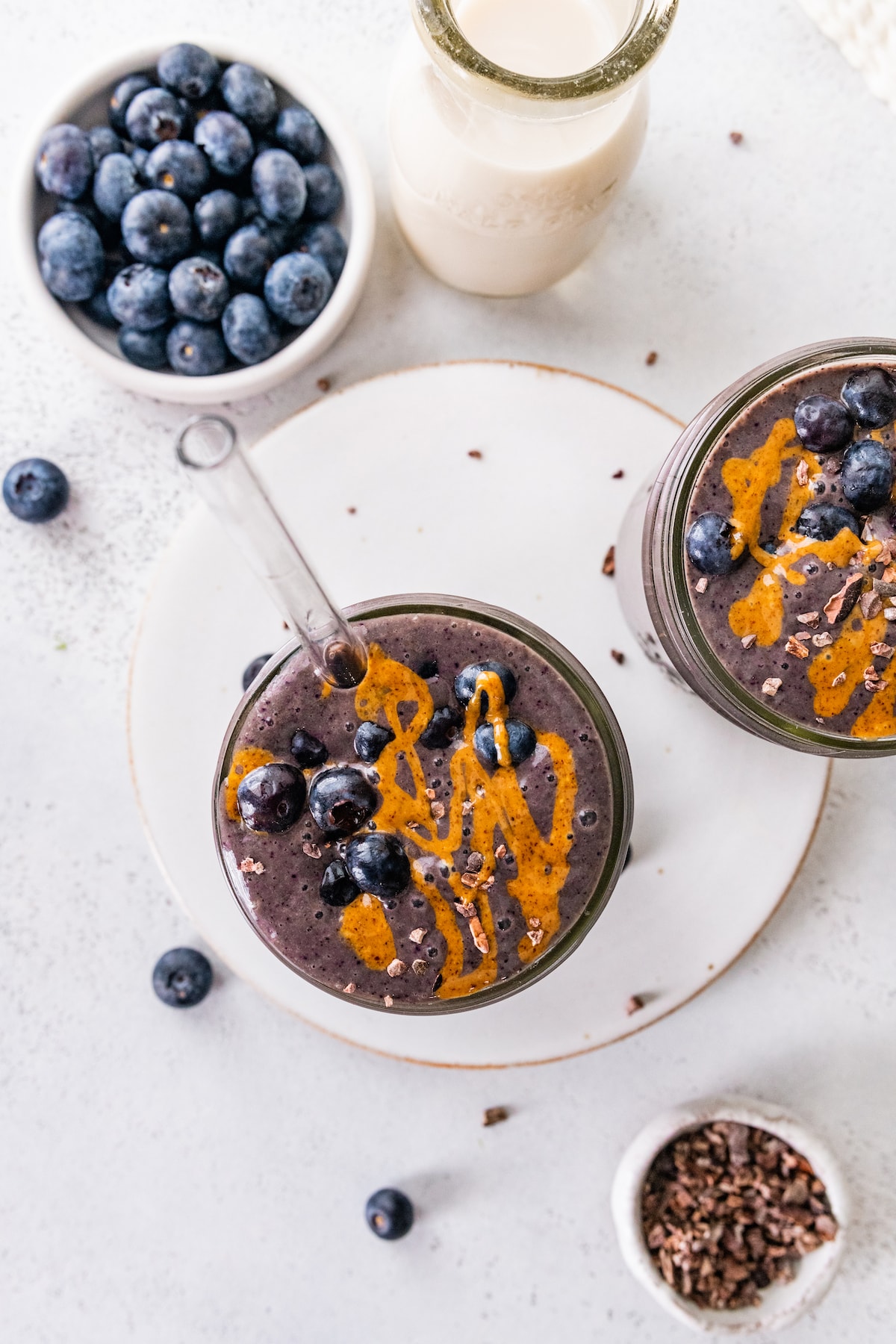Overhead image of two chocolate blueberry smoothies topped off with fresh blueberries and a drizzle of almond butter.
