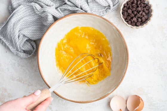 A woman's hand using a metal whisk to whisk the wet ingredients of the coconut flour cookies.