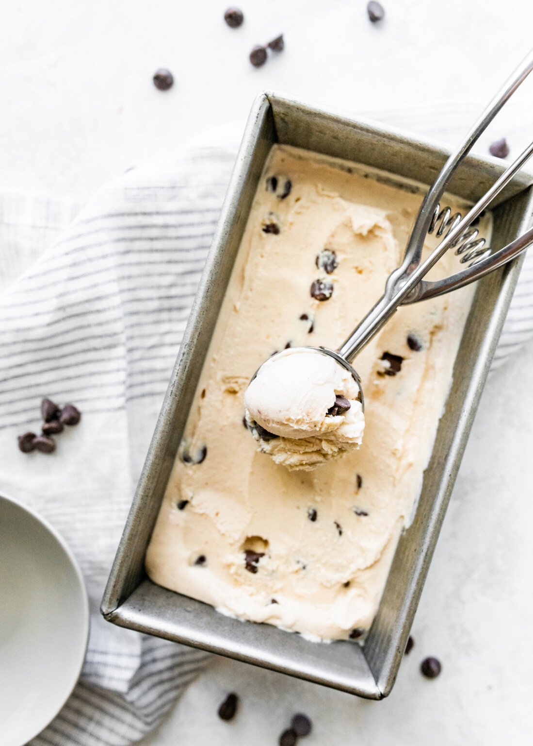 Pan of chocolate chip cottage cheese ice cream with a full ice cream scoop inside.