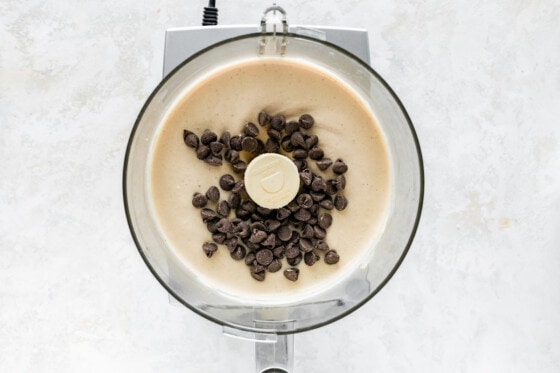 Chocolate chips being added to blended cottage cheese ice cream in a food processor.