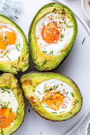On a white plate, two halved avocados with an egg in the center, each recently baked.