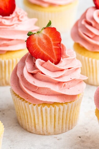 A cupcake with a pink strawberry buttercream frosting and a halved strawberry on top.