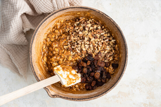 A large mixing bowl with a silicon spatula featuring the mixed batter for the healthy banana oat bars with walnuts and raisins ready to be mixed in.