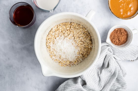A large white mixing bowl with oats and coconut shreds.