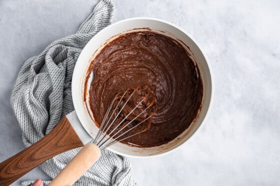 A white saucepan with a metal whisk and a chocolate mixture.