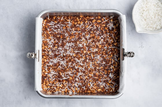 A square baking dish containing the no-bake chocolate coconut bars before being cut.