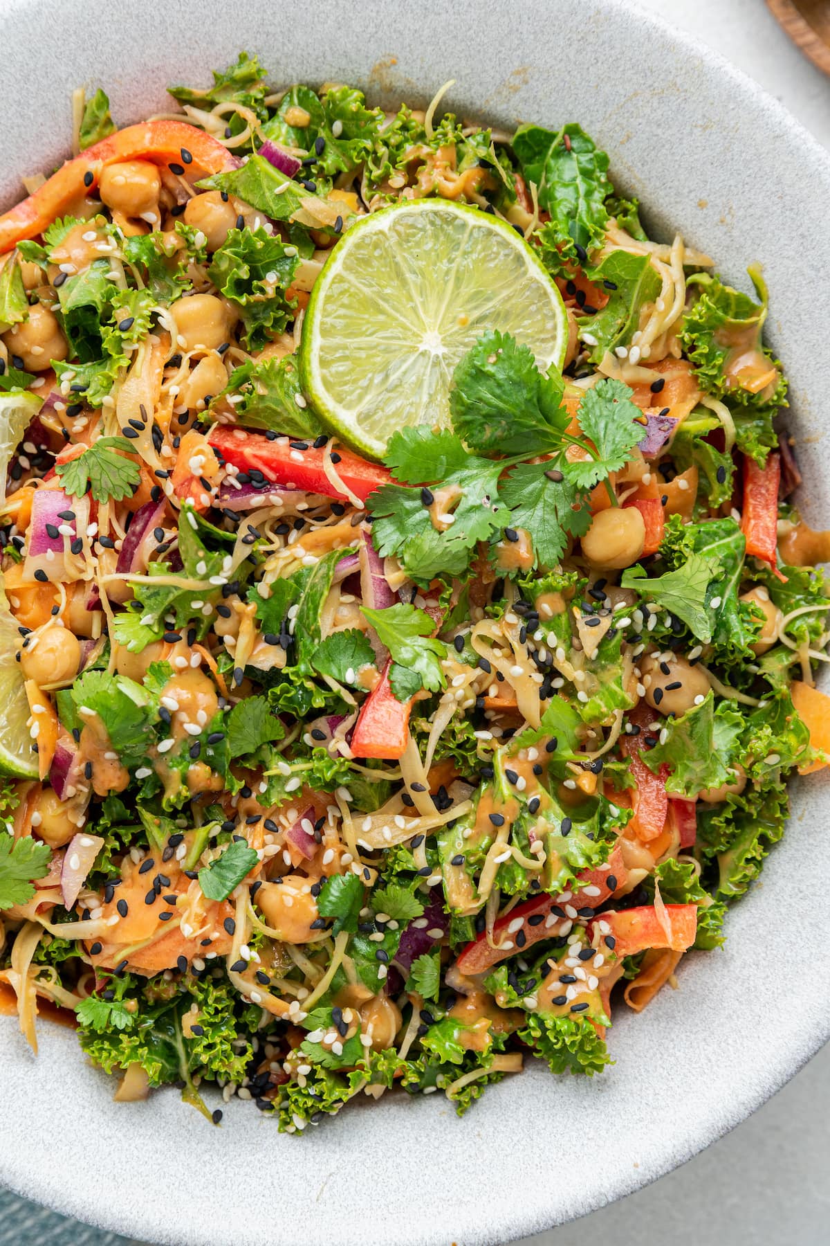 A white bowl with a colorful kale and cabbage pad thai salad and a lime wedge.