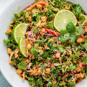 A white bowl with the kale and cabbage pad thai salad and a few lime wedges on top.