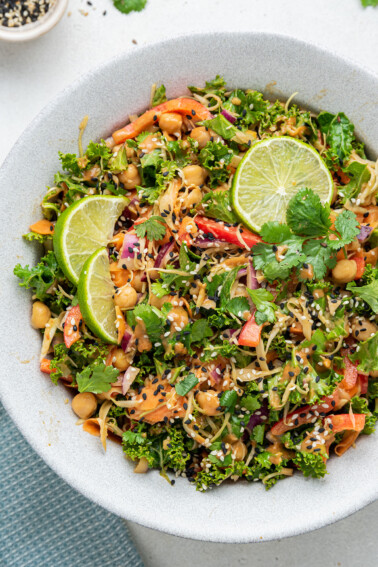 A white bowl with the kale and cabbage pad thai salad and a few lime wedges on top.