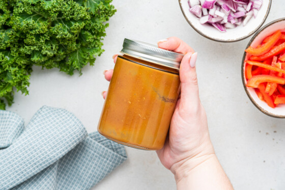 A woman's hand holding a jar with a pad thai salad dressing.