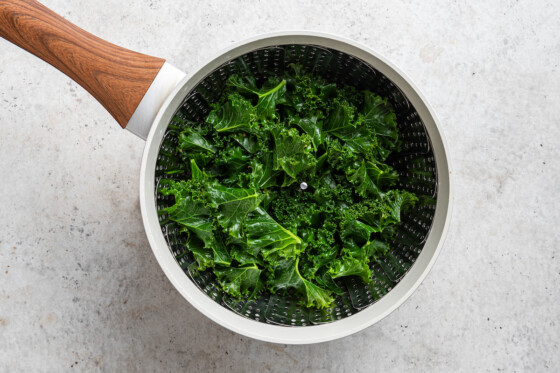 A metal colander with kale inside.