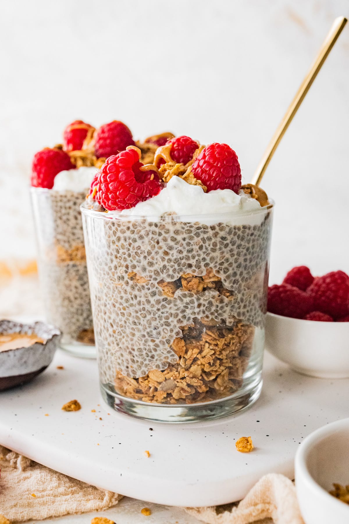 A jar of protein chia pudding topped with fresh raspberries, greek yogurt and a drizzle of nut butter.