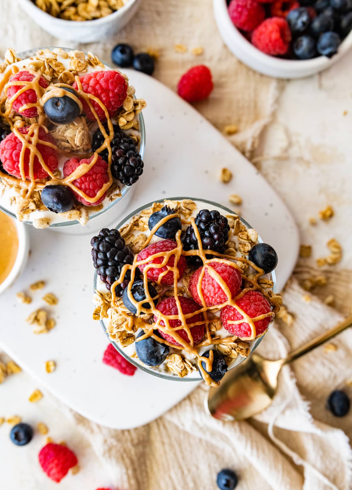 Two jars of protein chia pudding topped with fresh raspberries, blueberries, blackberries, greek yogurt and a drizzle of nut butter.