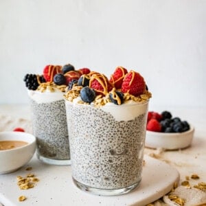 Two protein chia pudding jars topped with fresh raspberries, blueberries, blackberries, greek yogurt and a drizzle of nut butter.