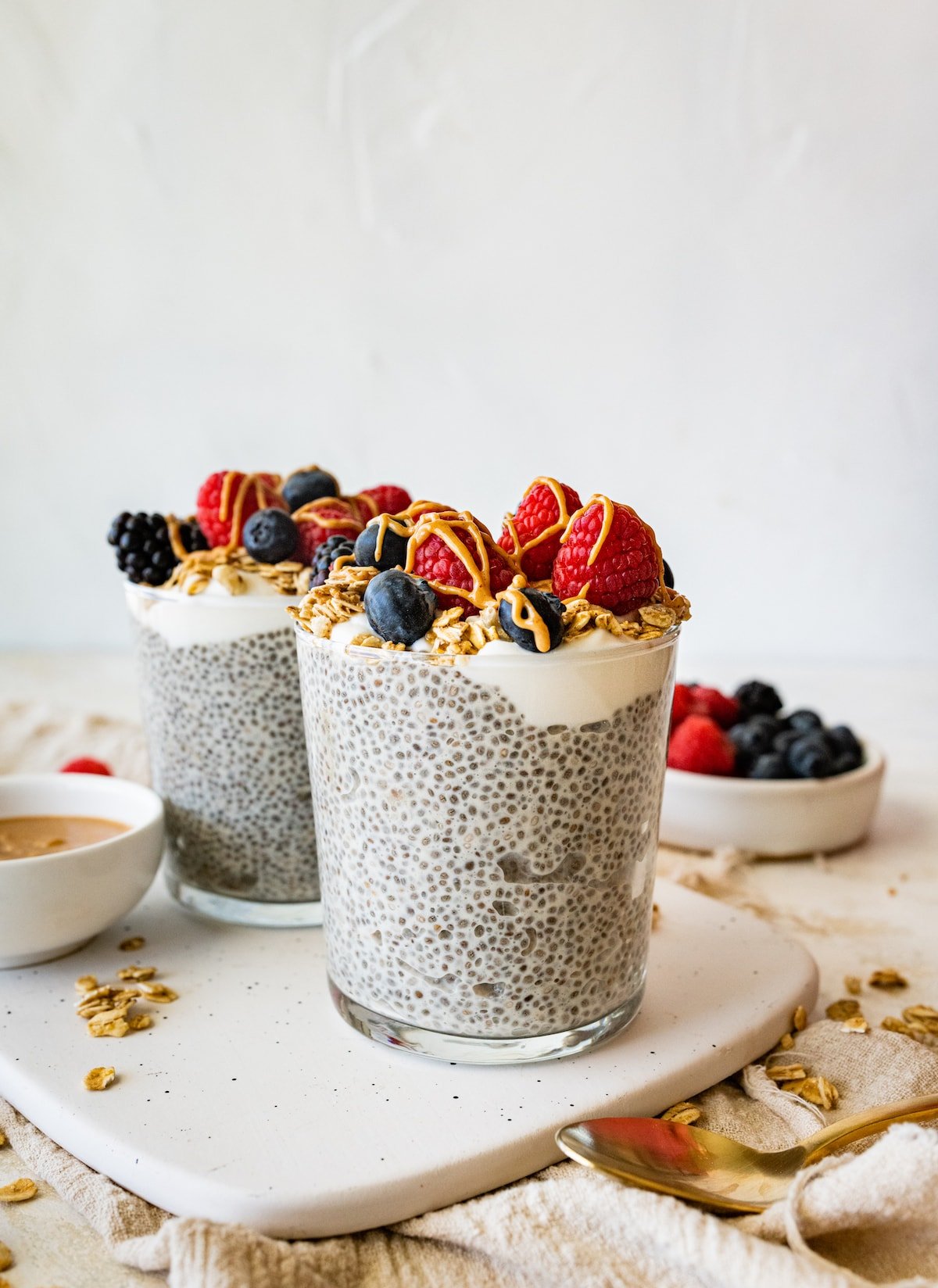 Two protein chia pudding jars topped with fresh raspberries, blueberries, blackberries, greek yogurt and a drizzle of nut butter.