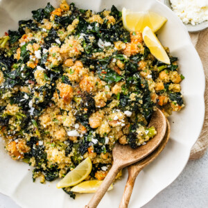 Roasted broccoli quinoa salad in a large white bowl with two wooden serving spoons.