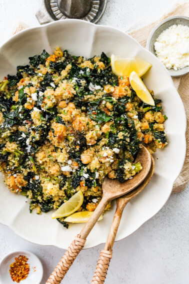 Roasted broccoli quinoa salad in a large white bowl with two wooden serving spoons.