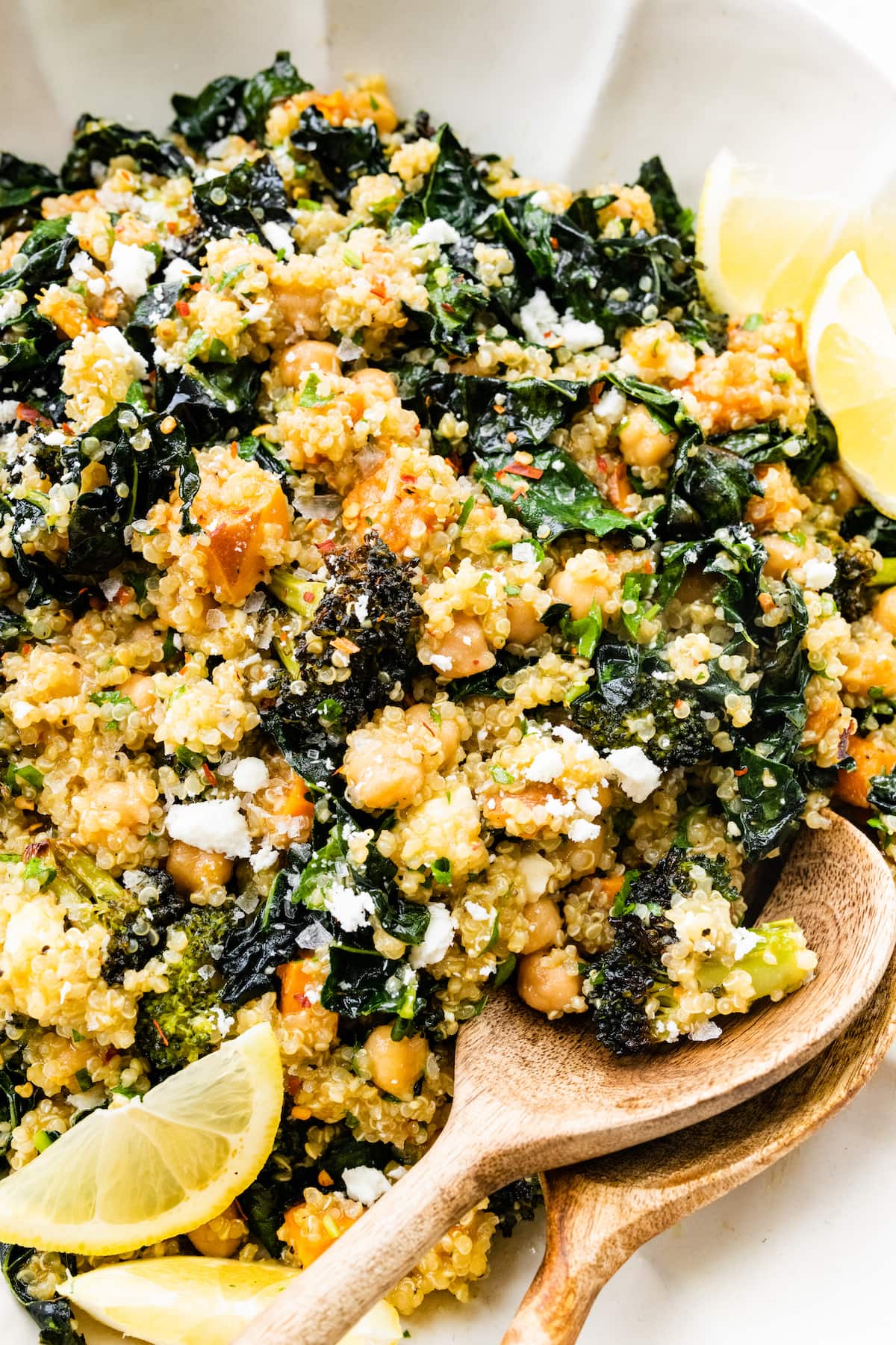 Roasted broccoli quinoa salad in a large white bowl with two wooden serving spoons.