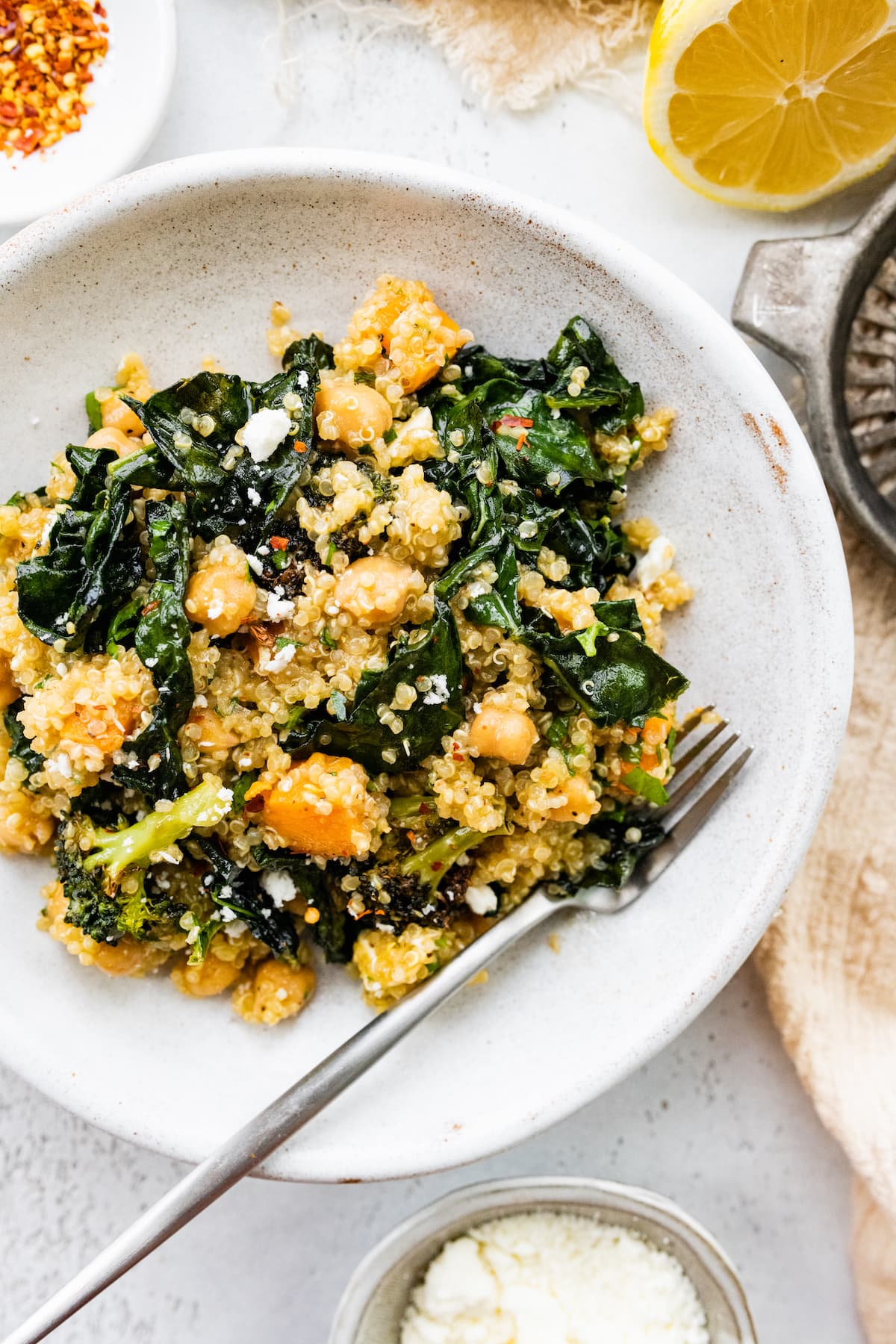 A white plate with a metal fork and a roasted broccoli quinoa salad serving.