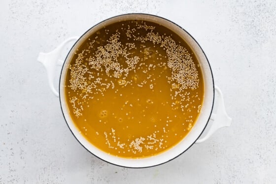 A large white pot with broth and uncooked quinoa.