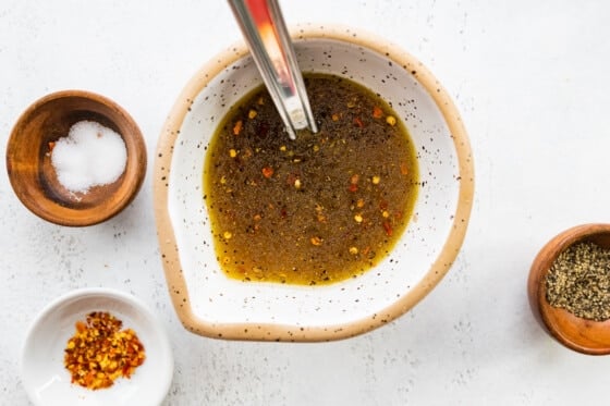 A small bowl containing lemon juice, vinegar, maple syrup, oil, salt, pepper, and crushed red pepper. Used as a dressing for the roasted broccoli quinoa salad.