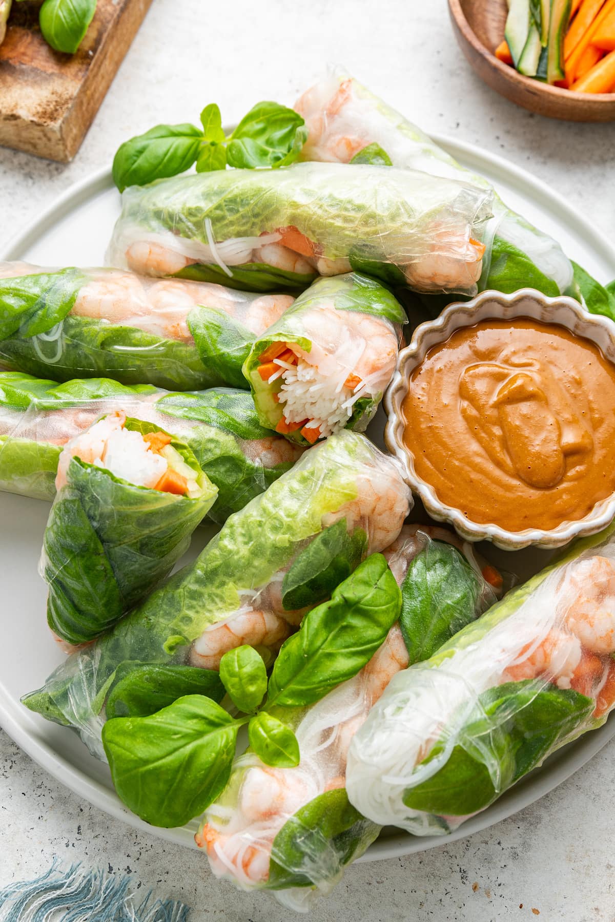 A large white plate with chopsticks containing multiple shrimp spring rolls, some cut in half, and a peanut sauce in a small white bowl.