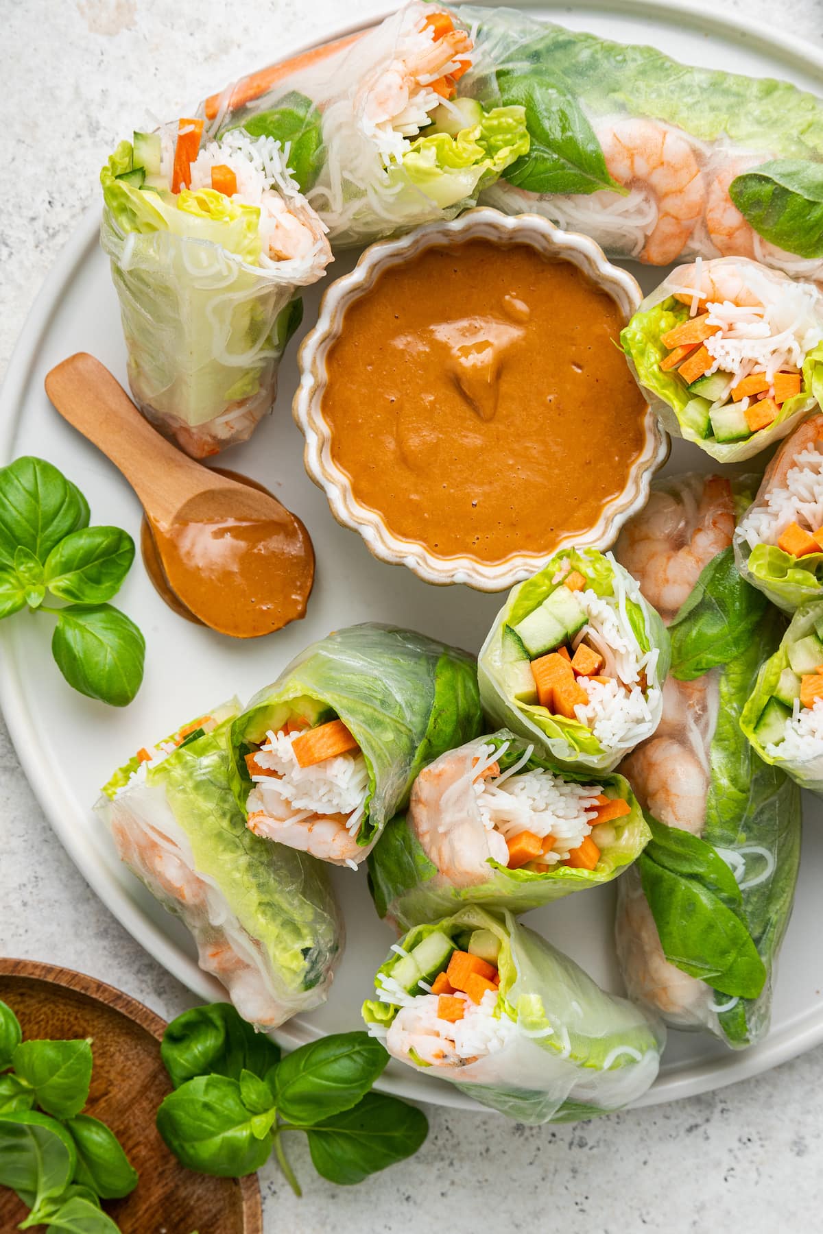 A large white plate containing multiple shrimp spring rolls, some cut in half, and a peanut sauce in a small white bowl.